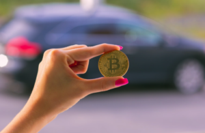 Mão segurando moeda de bitcoin com carro de fundo